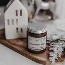 Kép betöltése a galériamegjelenítőbe: Christmas Tree szójagyertya fa tálcán, fenyőágakkal és tobozokkal körülvéve, ünnepi háttérrel.