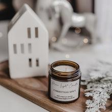 Kép betöltése a galériamegjelenítőbe: Christmas Spice szójagyertya fa tálcán, karácsonyi fűszerekkel és narancsszeletekkel körülvéve.