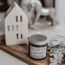 Kép betöltése a galériamegjelenítőbe: Merry Berry szójagyertya fa tálcán, friss szilvával és vaníliarúddal körülvéve, ünnepi hangulatú háttérrel.